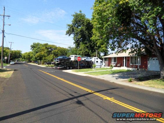 Car carrier truck loaded with a dark sedan, a white van, and another white vehicle, parked on a residential street
