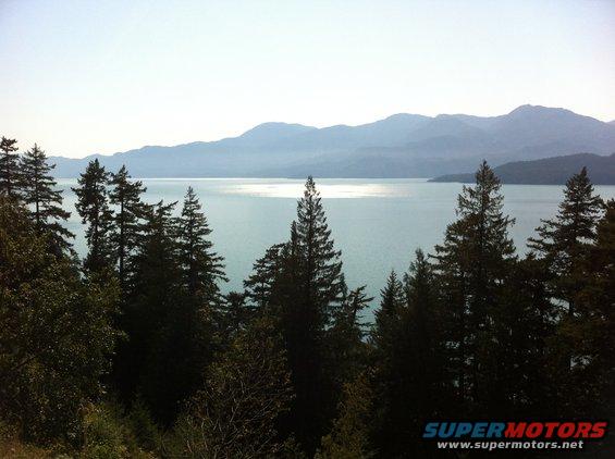 Water reflects sunlight between forested hills and distant mountains