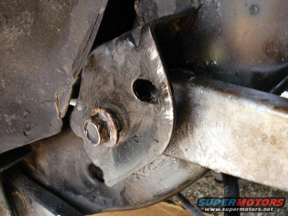 Close-up of a metal car suspension component with a bolt and stamped text 'FRONT'