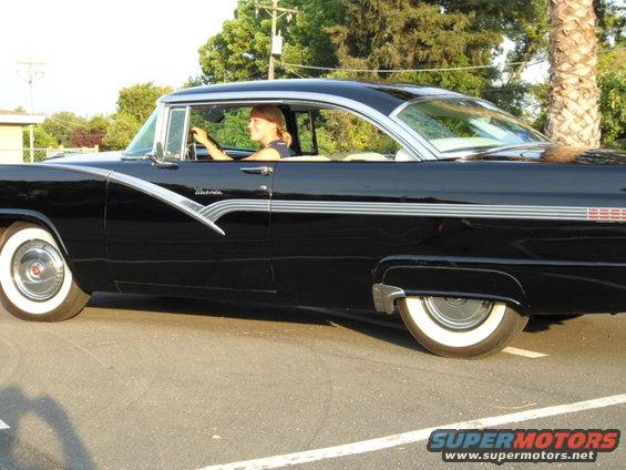 Black 1956 Ford Fairlane coupe, side view, woman driving