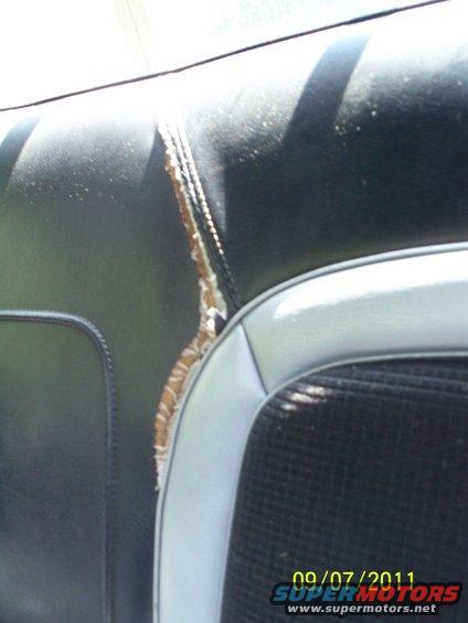 Close-up of ripped black vinyl seat with light blue trim and black fabric insert