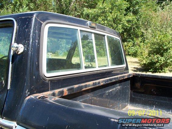 Black 1973 Ford F-100 pickup truck rear cab with sliding window, showing rust on bed rails