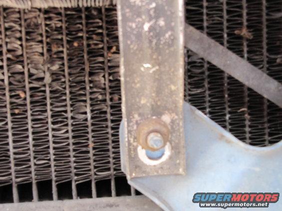 Close-up of a vehicle radiator with a metal mounting bracket and bolt