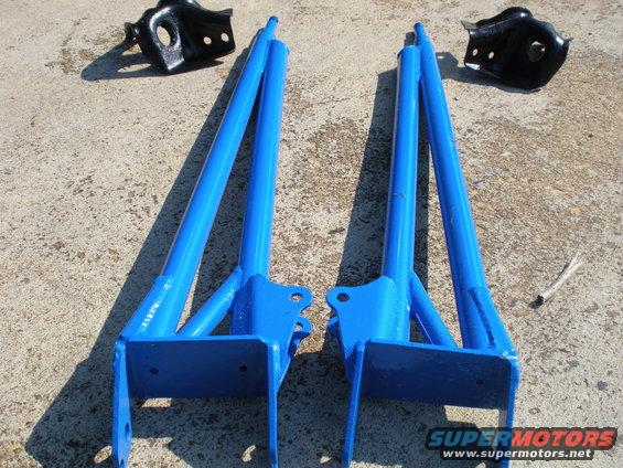 Two blue painted lift kit components and two black brackets on a concrete surface