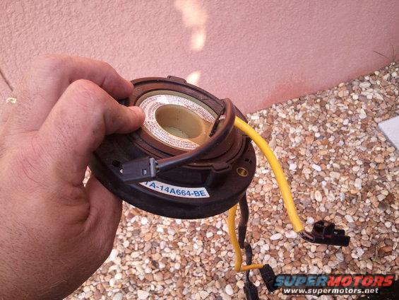 Hand holding a car clock spring part with yellow wire and connectors