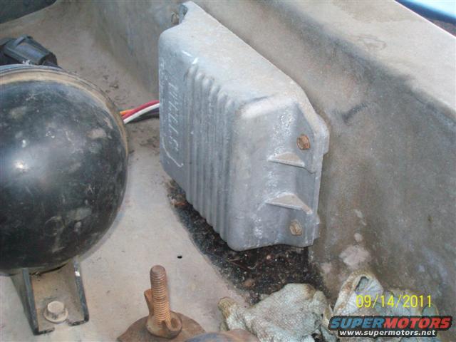 Close-up of a gray metal engine component with wires connected, next to a black round object