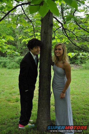 Young man in a suit and young woman in a gray dress stand by a tree