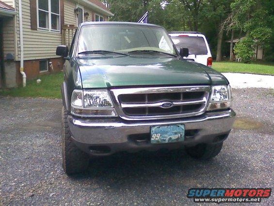 Green Ford Ranger pickup truck parked in gravel driveway, white SUV in background