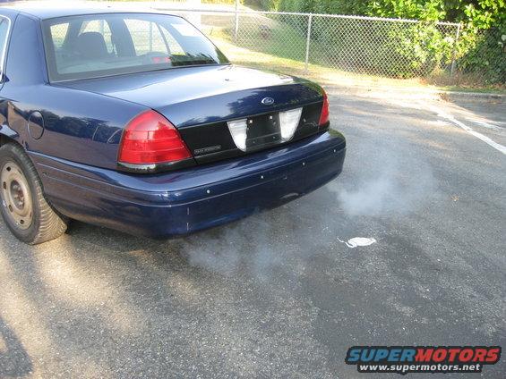 Blue 2003 Ford Crown Victoria emitting smoke from the exhaust, viewed from the rear quarter