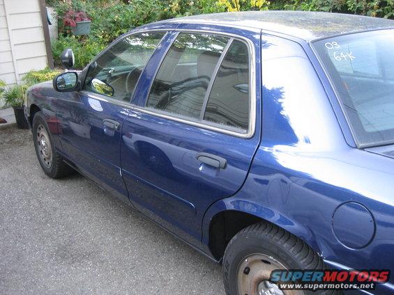 Blue sedan, 2003 Ford Crown Victoria, parked on asphalt, side view, with visible '03' marking on the rear quarter panel