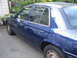 2003 Ford Crown Victoria - A blue 2003 Ford Crown Victoria is seen from the side, parked outdoors with some foliage in the background.