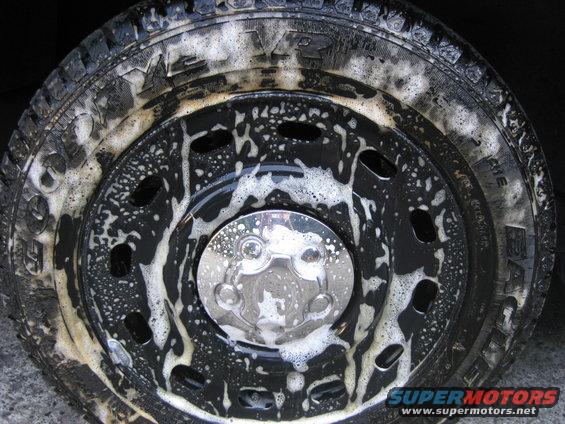 Close-up of a soapy truck wheel and tire with a chrome hubcap