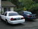 2003 Ford Crown Victoria - Two Ford Crown Victoria police interceptors are parked side-by-side in a residential driveway.
