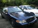 2003 Ford Crown Victoria - Two Ford Crown Victorias, one dark blue and one white, are parked outdoors.