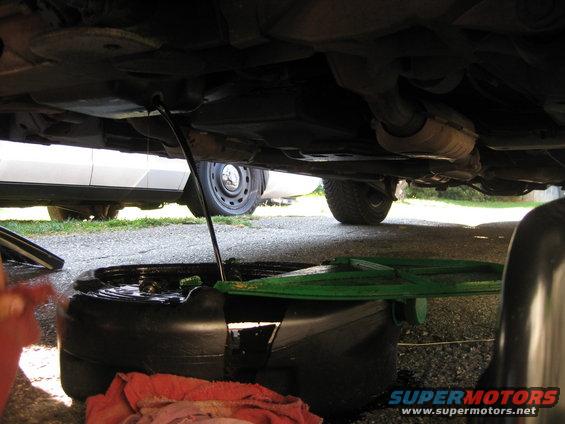 Underside of a car with oil draining into a pan, another car visible in background