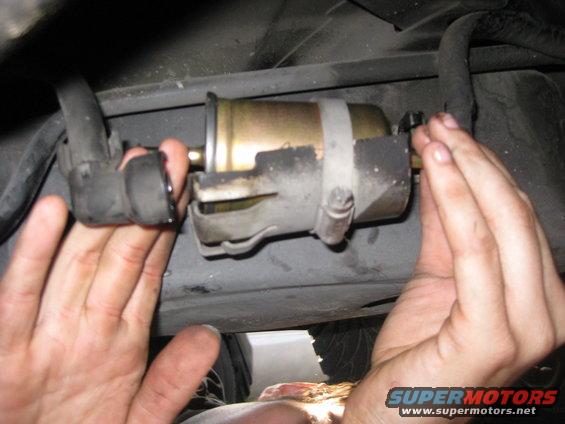 Hands replacing a car's fuel filter, showing hoses and mounting bracket