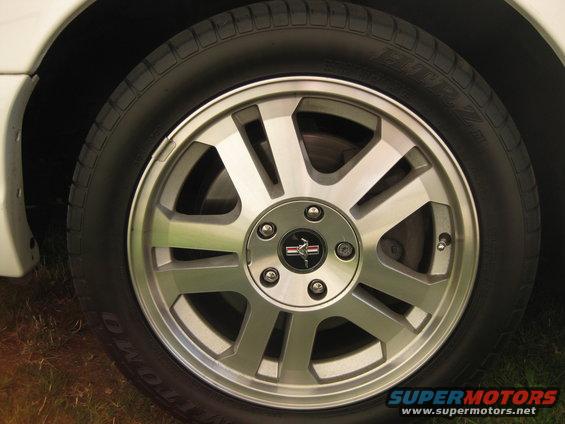 White car's front wheel with a silver alloy rim and a Mustang emblem