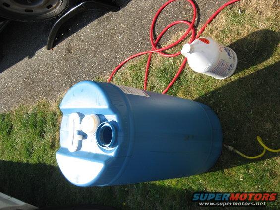 Blue barrel on grass with red hose connected to a white jug and yellow hose connected to the barrel