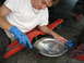 2003 Ford Crown Victoria - A person cleans a differential cover with a scraper, wearing blue gloves.