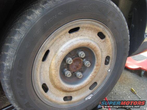 Rusty steel wheel with five lug nuts and a Goodyear tire