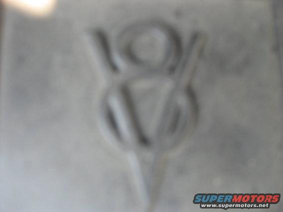 Embossed V8 emblem on a gray, textured surface