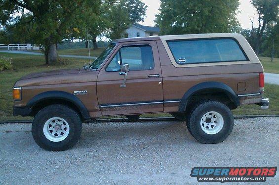 Brown 1987 Ford Bronco with a tan removable top, side view, lifted suspension, white rims