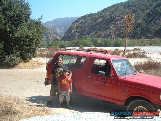Red 1987 Ford Bronco parked on a dirt road with two people standing next to it