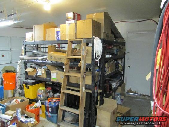 Garage shelves packed with boxes, buckets, and supplies. A wooden ladder leans against the shelves