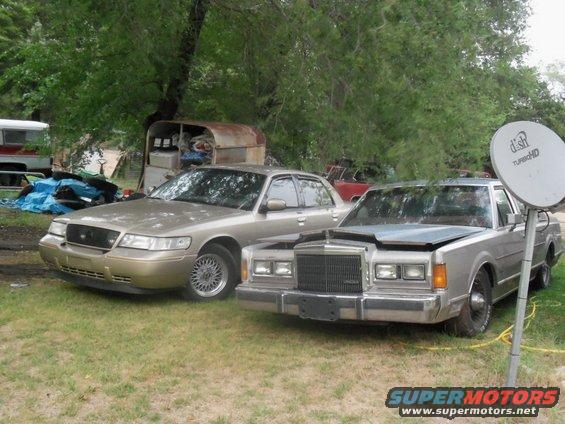 Gold sedan with a black grille and chrome wheels, parked next to a silver sedan with its hood open