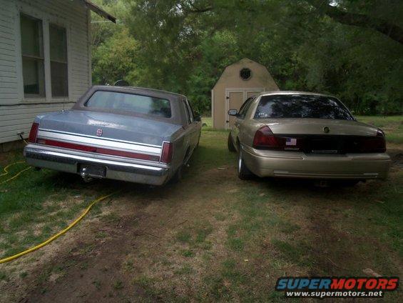 Gold sedan and a blue sedan parked in a grassy yard next to a house and shed