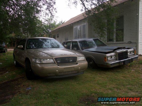 Gold sedan in front, older gray sedan with hood up behind it. Both parked on grass near a house