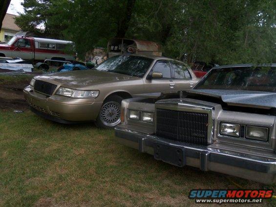 Gold sedan with a black grille and mesh wheels, parked next to a silver sedan with a chrome grille. Both are seen from the front