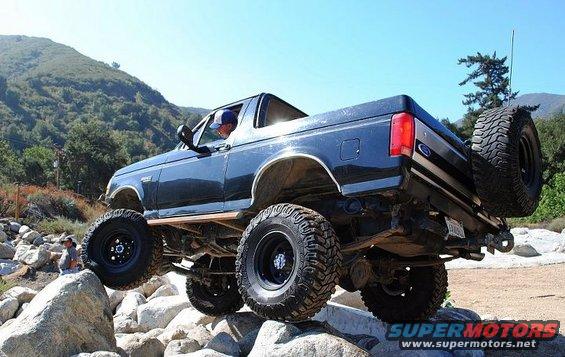 Dark blue 1992 Ford Bronco with lifted suspension and large off-road tires navigating rocks