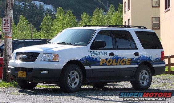 White police SUV with 'Whittier POLICE' text and mountain graphics on the side. License plate is yellow