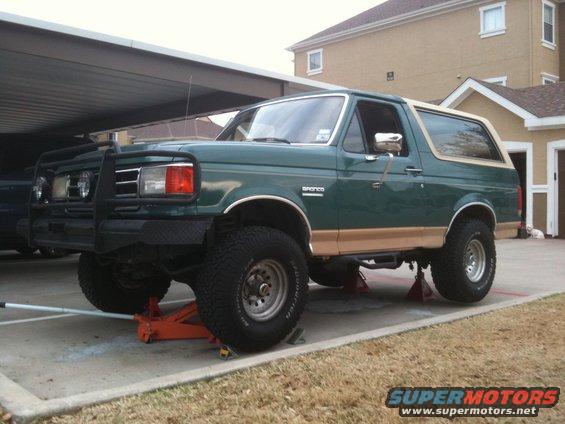 Green 1989 Ford Bronco with tan trim, lifted and on jack stands