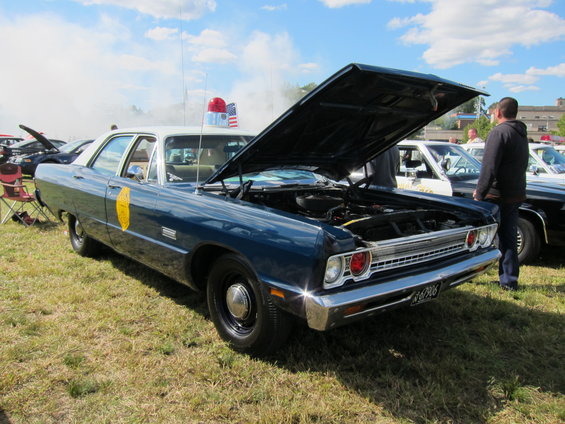 Blue police car with hood open, red and blue light bar on roof. Another police car is behind it