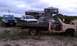 1979 Ford Bronco - Several trucks and a flatbed trailer are parked on a sandy area near a house on a cloudy day.