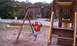 1979 Ford Bronco - A person enjoys a swing on a wooden playground set with a white picket fence in the background.