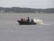 1979 Ford Bronco - A boat carrying three individuals speeds across the water, leaving a significant wake behind it.