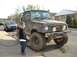 1986 Ford Bronco - A child stands next to a dirty Suzuki Samurai, with a residential street and houses visible in the background.