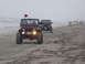 1979 Ford Bronco - A convoy of Jeeps, including a red Wrangler with a flag, cruises along a foggy beach.