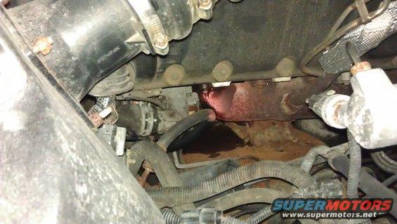 Engine bay showing exhaust manifold with red fluid leak and various hoses and wiring