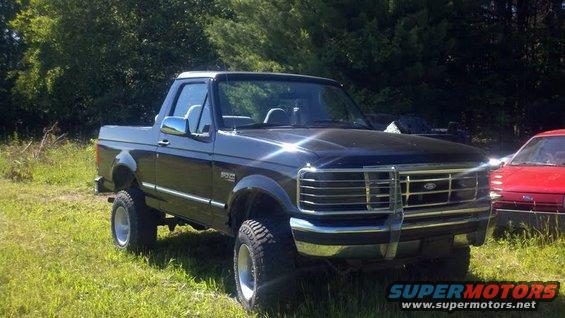Black 1995 Ford Bronco parked in grass with a red car to the right