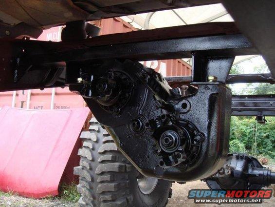 Close-up of a vehicle's transfer case and drivetrain components. A large red hood is visible to the left