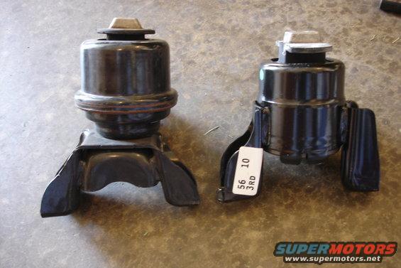 Two black engine mounts on a concrete surface. One mount is larger than the other. A white label on the smaller mount reads '56 3RD 10'
