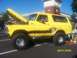 1989 Ford Bronco - A yellow Ford Bronco with custom graphics and a lifted suspension is parked outdoors with its hood open.