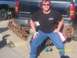 1989 Ford Bronco - A man poses with heavy chains attached to the rear of a black Chevrolet Silverado pickup truck.