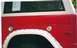 1974 Ford Bronco - The side of a red and white 1974 Ford Bronco is visible, with a white fender flare and a circular fuel cap.