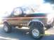 1989 Ford Bronco - This lifted Ford Bronco has a distinctive orange stripe and chrome wheels, parked in front of a food stand.