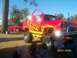 1989 Ford Bronco - A custom lifted SUV with flame graphics and open doors sits parked at an outdoor event, with another red truck visible in the background.